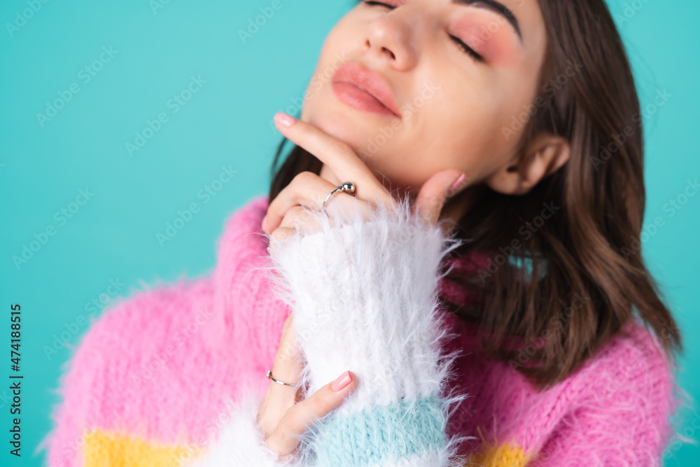 Close portrait of a young woman in a sweater on a blue background with graceful hands, long thin fingers, two cute silver rings, plump nude lips Close portrait of a young woman in a sweater on a blue background with graceful hands, long thin fingers, two cute silver rings, plump nude lips