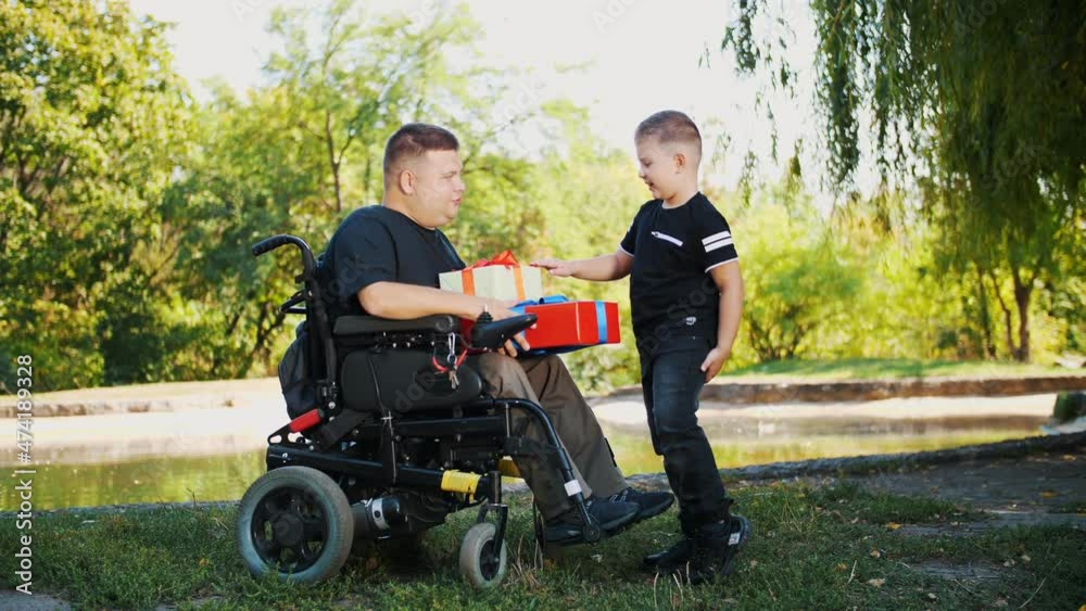 father's day. little cute boy gives gifts to his dad. a man is a person with disability. wheelchair user. people with special needs. father's day. little cute boy gives gifts to his dad. a man is a person with disability. wheelchair user. people with special needs.