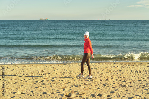 A woman in a red jumper and white hat walks along the sandy beach.  © NS
