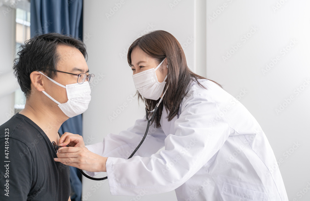 聴診器で診察するマスクをした笑顔の女医と男性患者