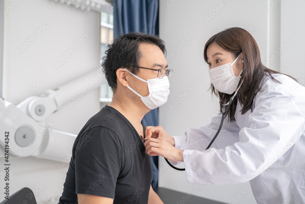 聴診器で診察するマスクをした女医と男性患者