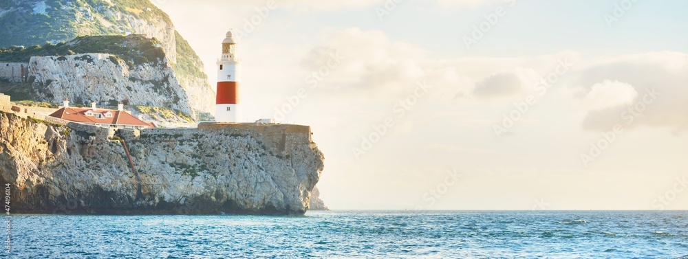 Trinity lighthouse at the rocky shore (cliffs) of the Europa Point. British Overseas Territory of Gibraltar, Mediterranean sea. Epic cloudscape. National landmark, sightseeing, travel destination - obrazy, fototapety, plakaty 