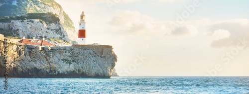 Trinity lighthouse at the rocky shore (cliffs) of the Europa Point. British Overseas Territory of Gibraltar, Mediterranean sea. Epic cloudscape. National landmark, sightseeing, travel destination