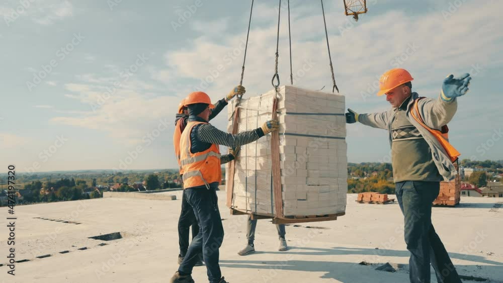 Male builders take bricks on the roof of the house. Construction of a multi-storey red brick house. A construction crane delivered bricks to the roof of the house.