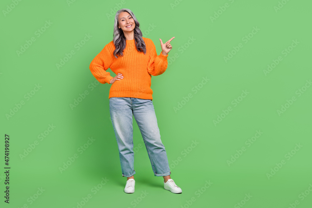 Full size photo of nice white plus size old lady index empty space wear sweater jeans shoes isolated on green color background Full size photo of nice white plus size old lady index empty space wear sweater jeans shoes isolated on green color background