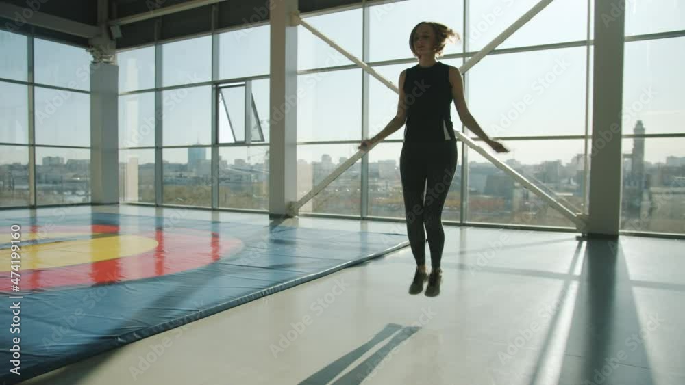 Young fit sportswoman wearing trendy outfit is jumping with skipping rope in modern gym. Active lifestyle and healthy youth concept. Young fit sportswoman wearing trendy outfit is jumping with skipping rope in modern gym. Active lifestyle and healthy youth concept.