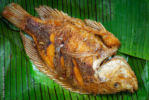 Close up top view shot of tilapia fish deep fried and displayed on green banana leaf before service with sauce. The famous fish dish in asia called sizzling fish.  