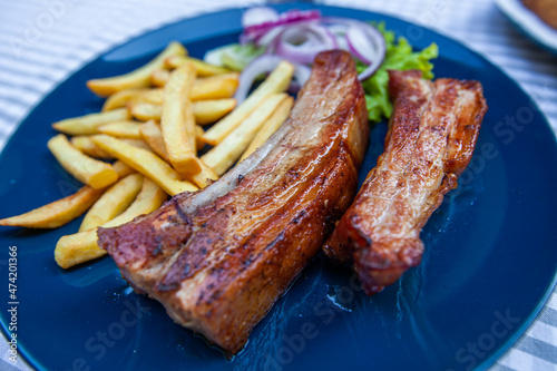Grilled pork ribs with French fries and onion. Serving on plate at restaurant table.