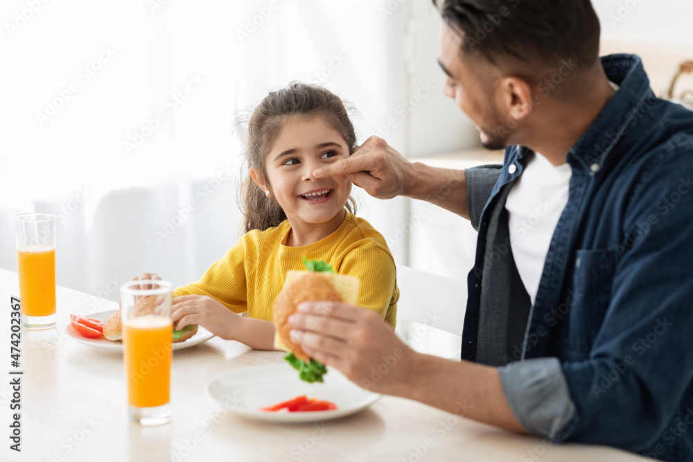 Portrait Of Cheerful Arab Dad And Little Daughter Having Lunch In Kitchen Portrait Of Cheerful Arab Dad And Little Daughter Having Lunch In Kitchen