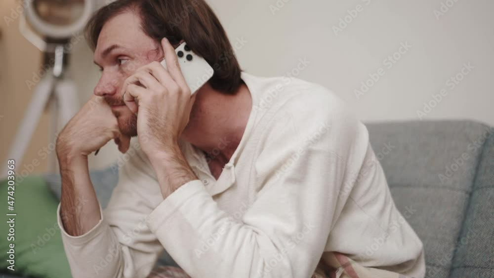 Sick man speaks on the phone and looks at a thermometer at home Sick man speaks on the phone and looks at a thermometer at home