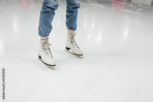 partial view of young woman in jeans skating on ice rink.