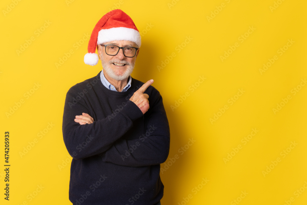 Senior smiling man wearing santa hat pointing finger up standing isolated over yellow background.