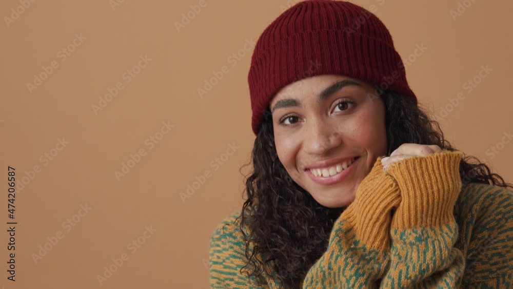 Smiling African curly-haired woman posing and looking to the side in beige studio Smiling African curly-haired woman posing and looking to the side in beige studio