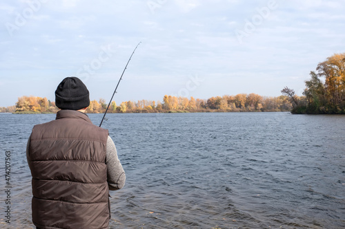 A fisherman stands on the bank of the river with a spinning rod in his hands and catches fish. The concept of a calm outdoor recreation