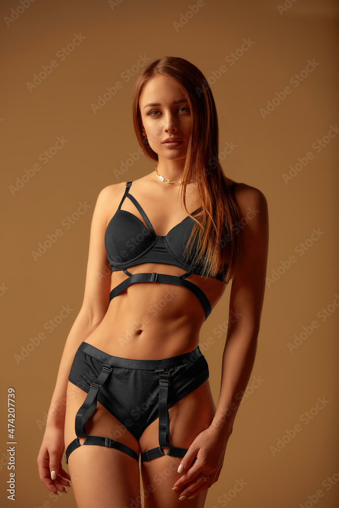 Fototapeta premium Young girl in black underwear with an ideal body, posing in the studio. Young woman with a beautiful and healthy body. Sexy woman with a perfect body.