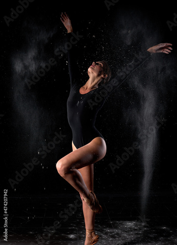 Dramatic portrait of young, strong and talented female dancer with white powder explosion, moving in dust, flour. Graceful caucasian slim gorgeous woman in black bodysuit in slow motion