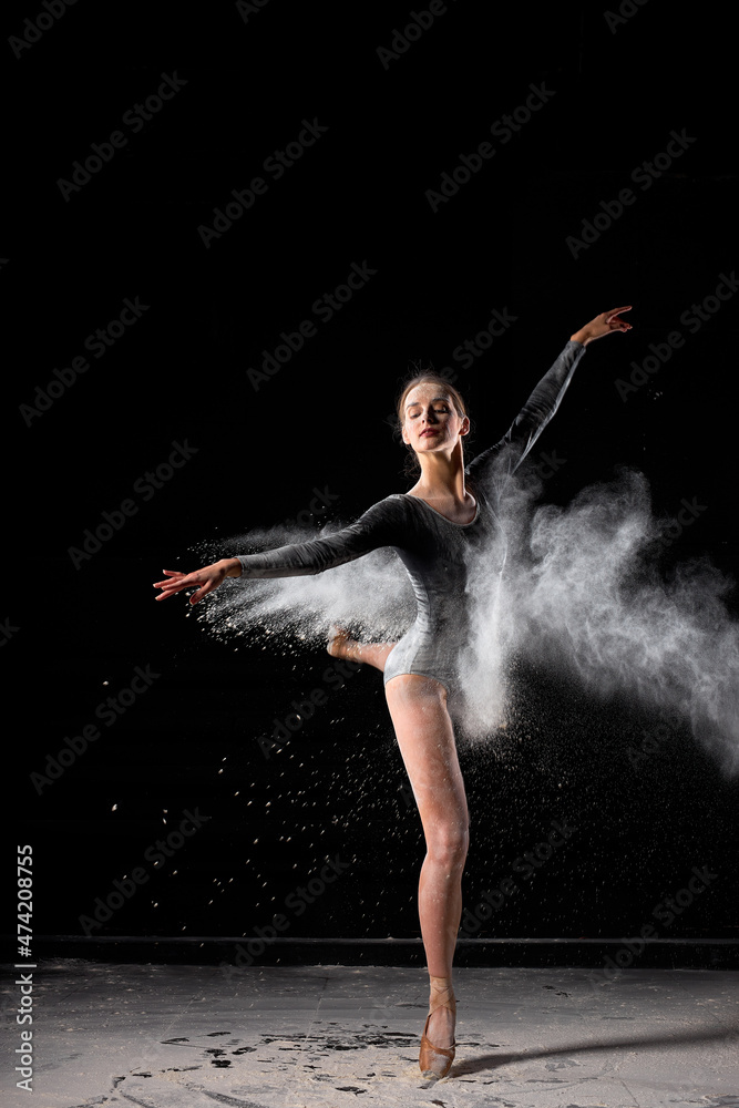 Beautiful ballerina woman in black bodysuit beautifully dances ballet in dark studio with flour on black background. Athlete female moving gracefully, talented ballet dancer alone. portrait. art