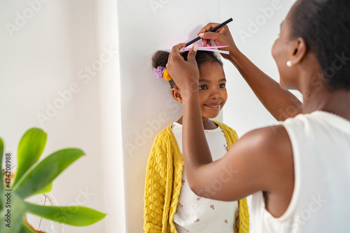 Mother measuring daughter's height and marking on wall at home photo