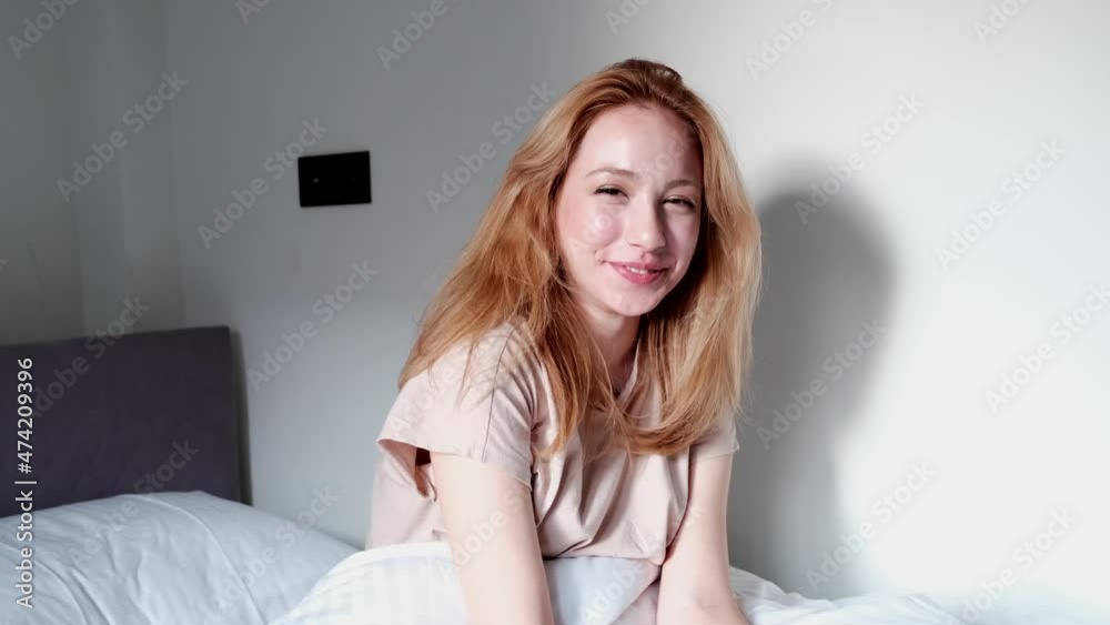 woman with positive feelings sitting on bed in pajamas and smiling at camera woman with positive feelings sitting on bed in pajamas and smiling at camera