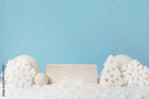 White cube pedestal on snow, winter festive blue background. Light Christmas scene with a podium. Display of cosmetics and beauty products. Stand with white New Year's decor