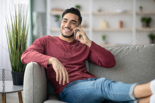 Happy middle-eastern guy reclining on couch, talking on phone