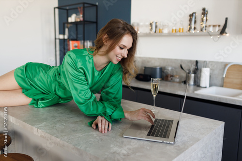 young smiling woman in fashiom dress at home with laptop and champagne photo