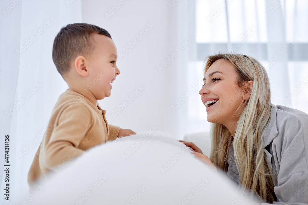 Happy american european family mom and child boy having good time on sofa. Young smiling female with cute son at home playing together, laughing, looking at each other. leisure time concept Happy american european family mom and child boy having good time on sofa. Young smiling female with cute son at home playing together, laughing, looking at each other. leisure time concept
