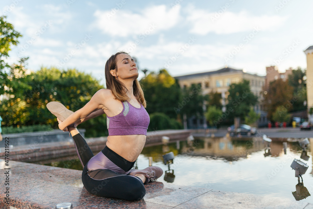 Beautiful girl in sportswear doing yoga poses on the sunset near  the fountain in the park , balance, fitness, stretching and relaxation.