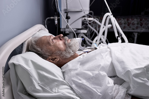 covid-19 patient with Endotracheal Tube In Mouth Lying On Medical Couch, Bed in hospital. senior sick person alone in ward room, suffering from disease. therapy, treatment, medicine concept photo