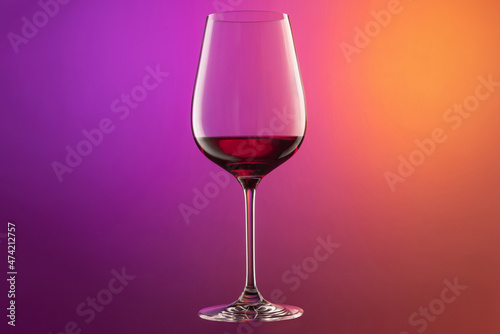 Close-up red wine glass isolated over gradient purple and orange color background in neon. Concept of alcohol, holidays, New Year