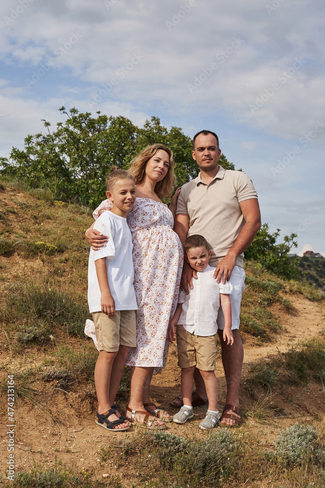 happy laughing family with two sons on a sunny summer day in nature against the blue sky descends the hill. mom is pregnant happy laughing family with two sons on a sunny summer day in nature against the blue sky descends the hill. mom is pregnant