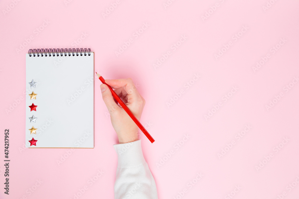 Female hand writing in white blank open spiral notebook with stars isolated on pastel pink background. Flat lay, copy space. Creative work, business, to do list or education concept. Female hand writing in white blank open spiral notebook with stars isolated on pastel pink background. Flat lay, copy space. Creative work, business, to do list or education concept.