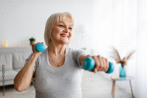 Tableau sur toile Mature woman exercising at home with two dumbbells