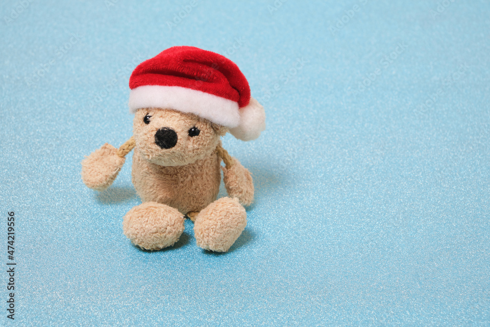 Stuffed teddy bear in a Santa Claus hat on a blue background.