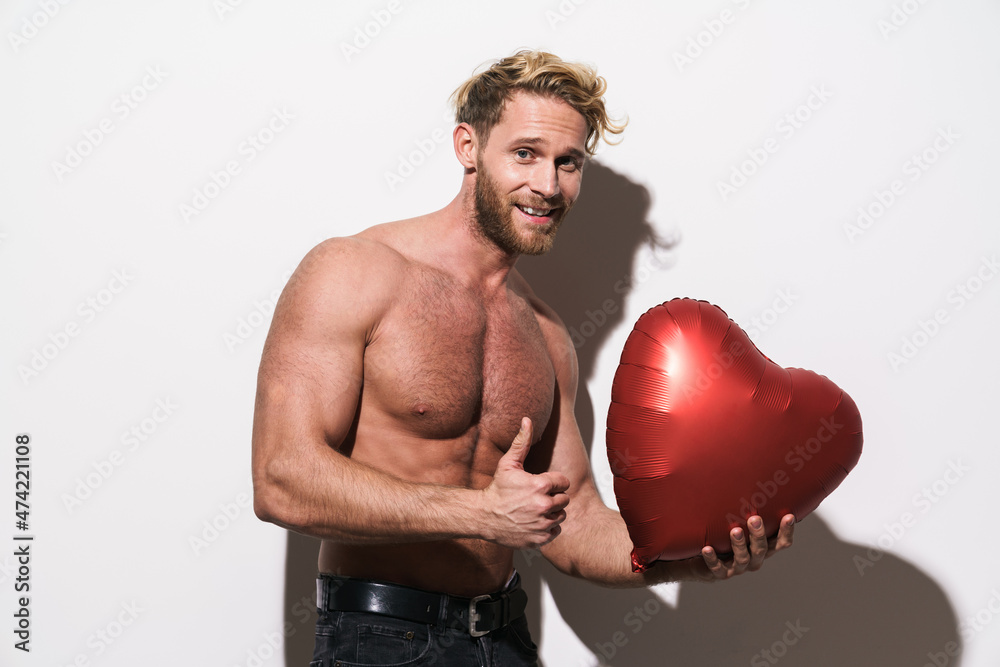 Shirtless man showing thumb up while posing with inflatable heart Shirtless man showing thumb up while posing with inflatable heart