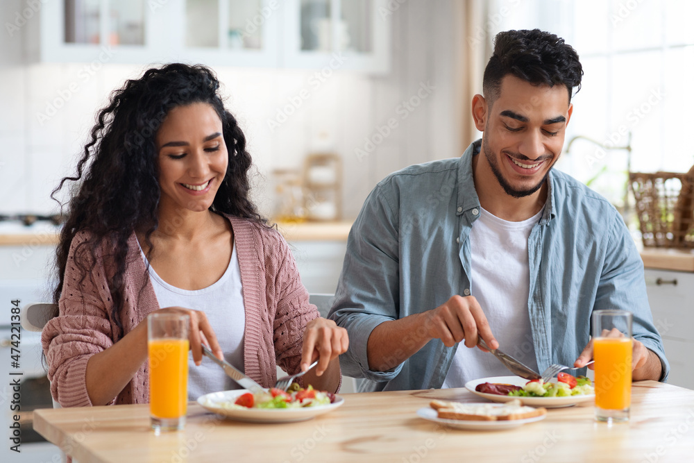 Couple's Daily Life. Happy middle eastern spouses eating breakfast in kitchen Couple's Daily Life. Happy middle eastern spouses eating breakfast in kitchen