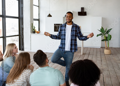 Happy black guy showing pantomime to his multiracial friends, playing charades guessing game at home