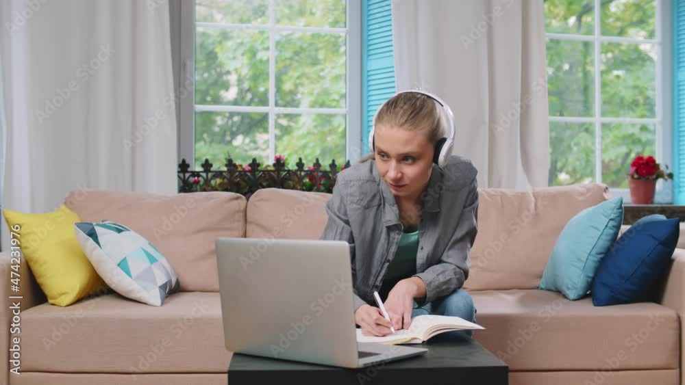 Young woman in headphones watching online webinar on laptop and writing notes at home. Realtime Young woman in headphones watching online webinar on laptop and writing notes at home. Realtime