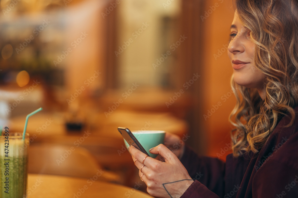 Beautiful young woman drinking coffee and using smartphone in a cafe