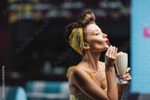 side view of young pin up woman drinking milkshake through straw.
