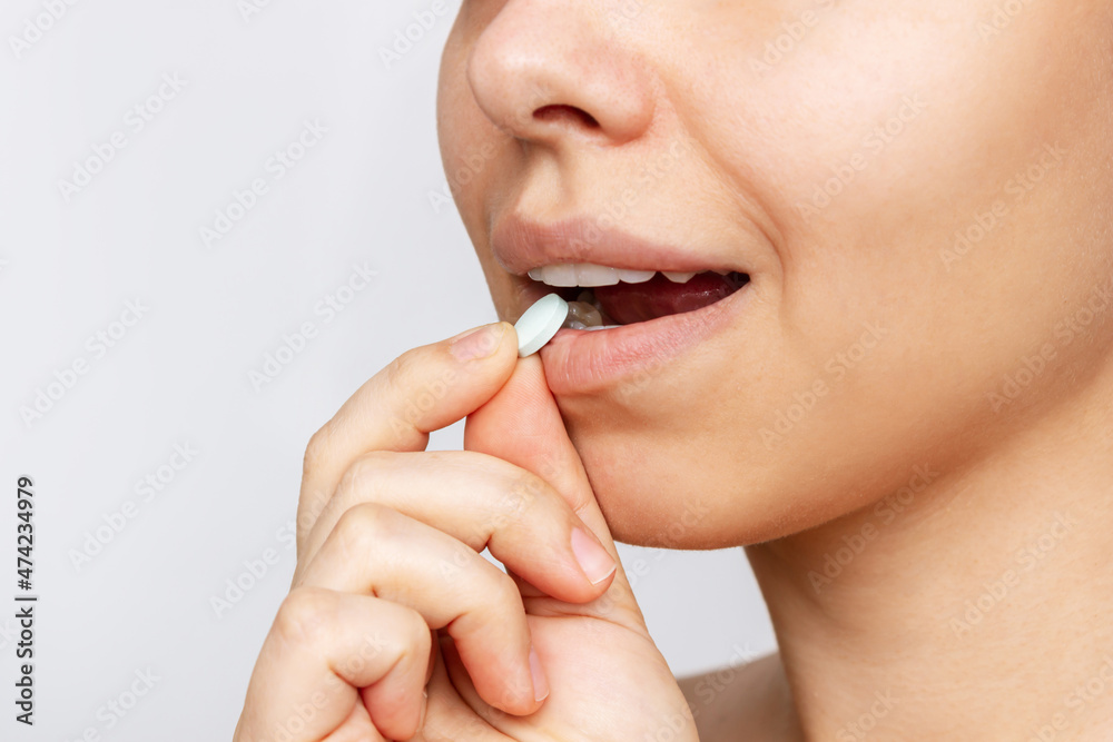 Cropped shot of a young caucasian woman taking a pill. The girl takes medications isolated on a white background. Treatment of the disease