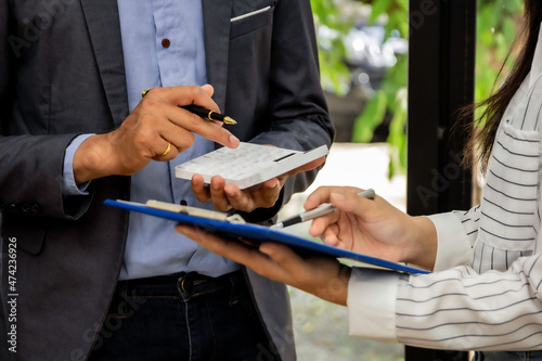 Male and female assistant finance managers stand in a conference room discussing money for the past month focusing on company expenses, accountants standing by looking at company unnecessary expenses.