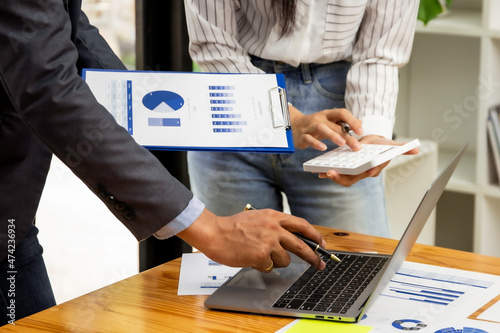 Male and female assistant finance managers stand in a conference room discussing money for the past month focusing on company expenses, accountants standing by looking at company unnecessary expenses.
