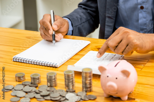 A businessman puts a coin in a piggy bank . A men saves money for household expenses. utility bills Monthly Family Budget Calculation Investment or personal savings strategy.
