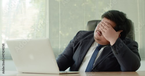 Asian business man which has a fat figure and funny personality, wearing a suit like an executive or a manager using a laptop in the office,feeling stressed and anxious about business. photo