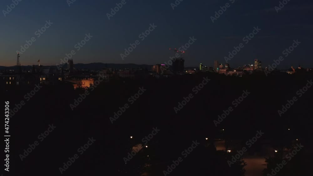 Evening fly above trees in park. Illuminated buildings in city after sunset. Clear sky at dusk. Evening fly above trees in park. Illuminated buildings in city after sunset. Clear sky at dusk.