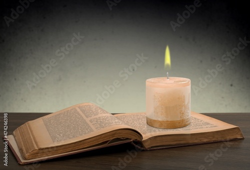 Vintage background with an old antique book, glasses and candle burning at night.