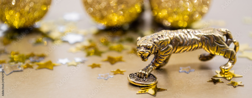 Banner with bronze figure of a tiger with a coin - the symbol of the Chinese new year 2022 on a background of golden stars, copy space. Wishes of good luck, financial well-being and wealth Banner with bronze figure of a tiger with a coin - the symbol of the Chinese new year 2022 on a background of golden stars, copy space. Wishes of good luck, financial well-being and wealth