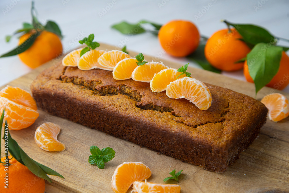 Vegan tangerine sponge cake with mandarin orange wedges on a wooden board.