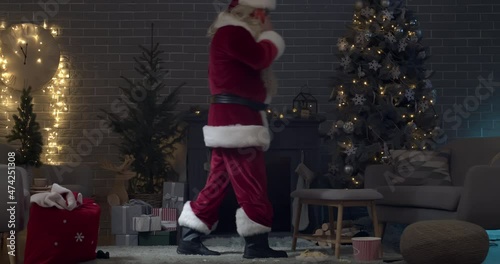 Santa Claus talking by phone in living room decorated for Christmas